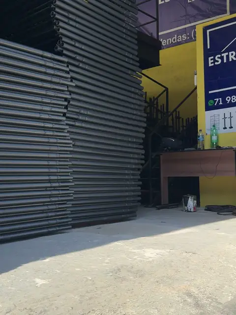 Pilhas de painéis de andaime tubular no térreo do galpão, com o banner da ESTRUTEC ao fundo