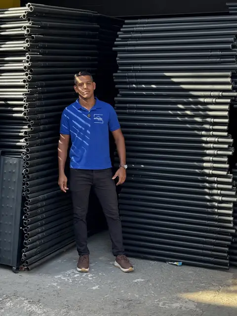Homem de camisa azul na frente das pilhas de painéis, no galpão da ESTRUTEC