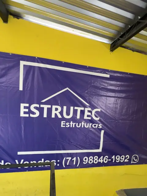 Banner da ESTRUTEC Estruturas com o número de vendas, na parede amarela do galpão